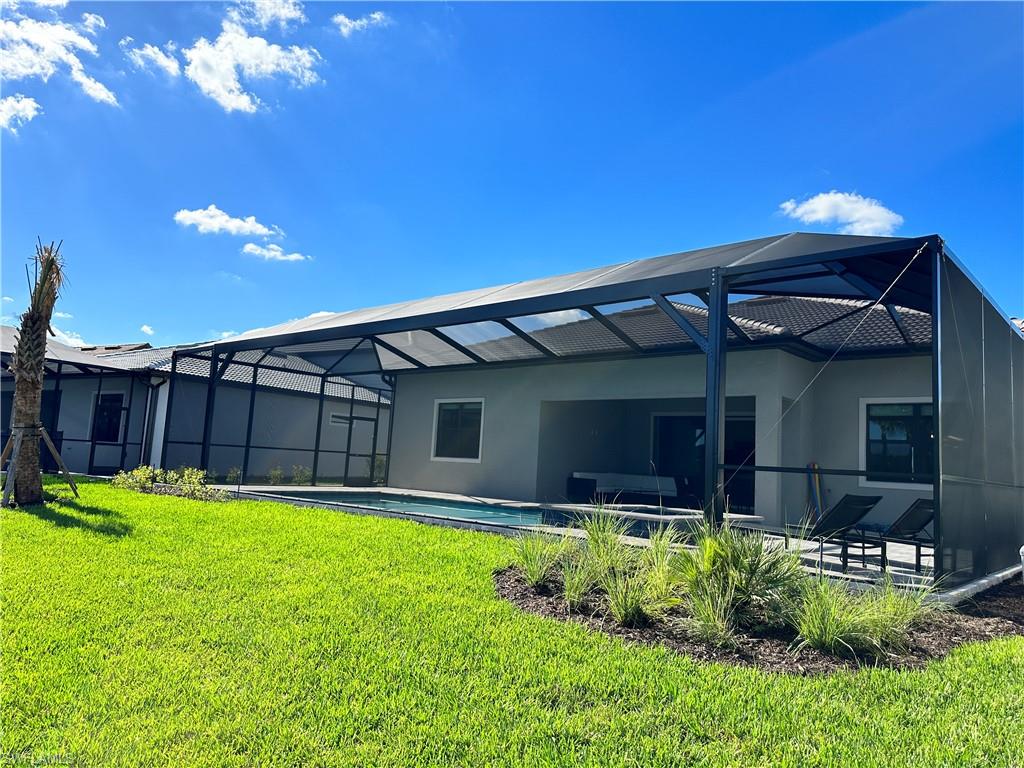 Rear view of property with a sunroom, a lanai, a lawn, an outdoor pool, and a patio area