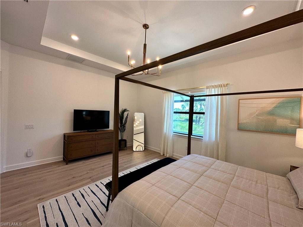 Bedroom with recessed lighting, wood finished floors, a chandelier, and a tray ceiling