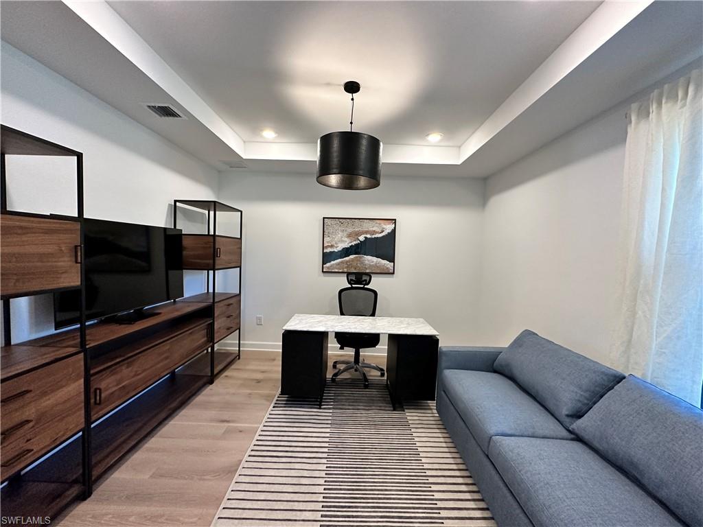 Office area with light wood-style floors, a tray ceiling, and recessed lighting