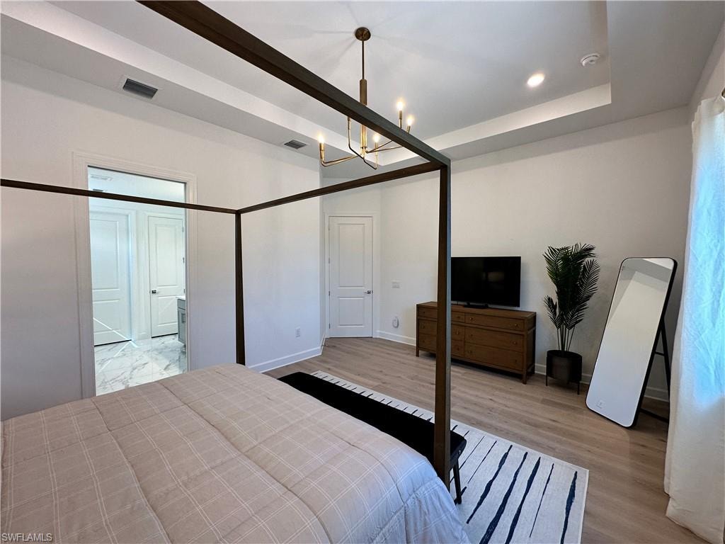 Bedroom with light wood finished floors, a chandelier, recessed lighting, and a raised ceiling