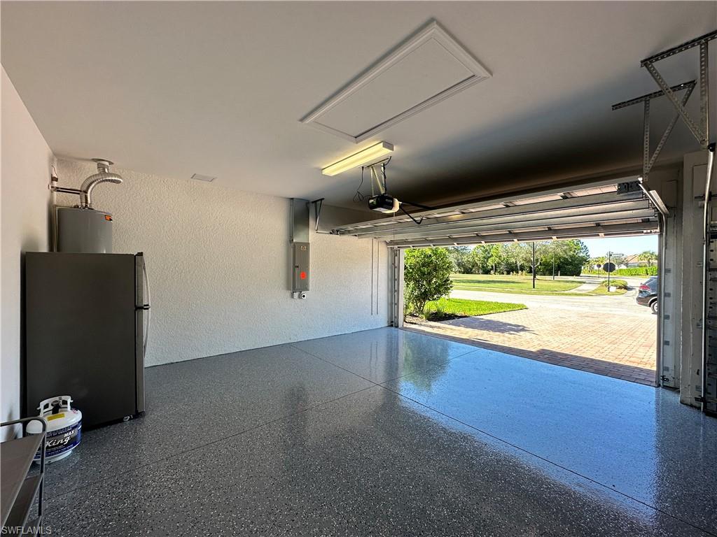 Garage featuring a textured wall, freestanding refrigerator, electric panel, and water heater