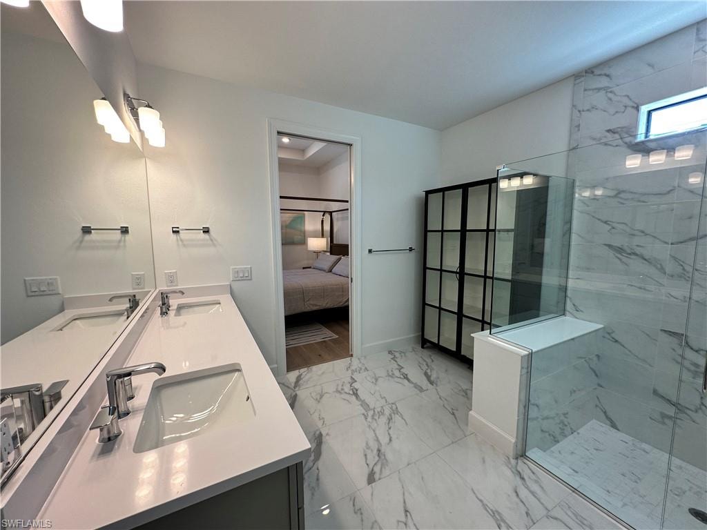 Ensuite bathroom featuring light marble finish floors, double vanity, and a marble finish shower