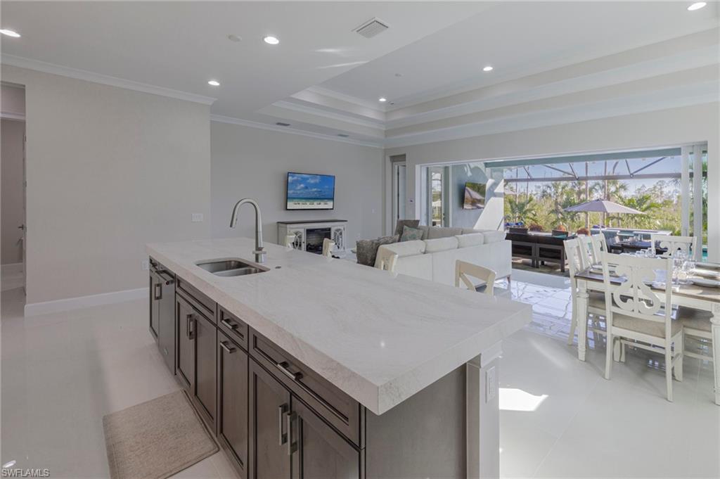 Kitchen featuring sink, crown molding, a tray ceiling, dark brown cabinets, and a center island with sink