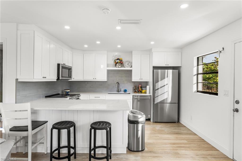 Kitchen with white cabinets, appliances with stainless steel finishes, a peninsula, a breakfast bar, and recessed lighting