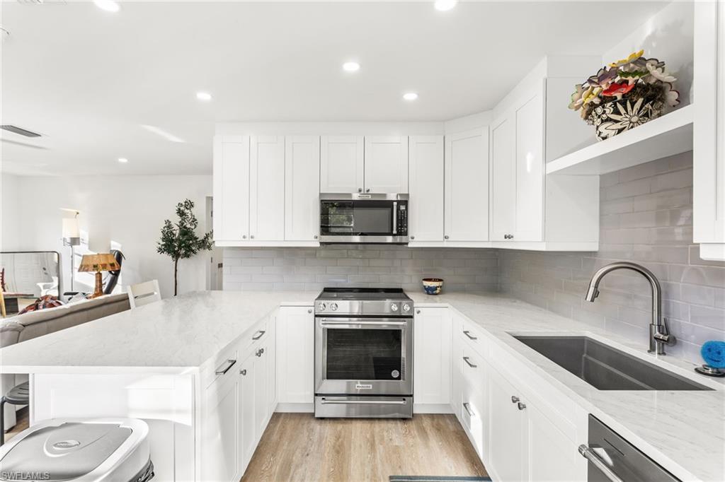 Kitchen featuring appliances with stainless steel finishes, light stone countertops, a breakfast bar area, white cabinets, and a peninsula