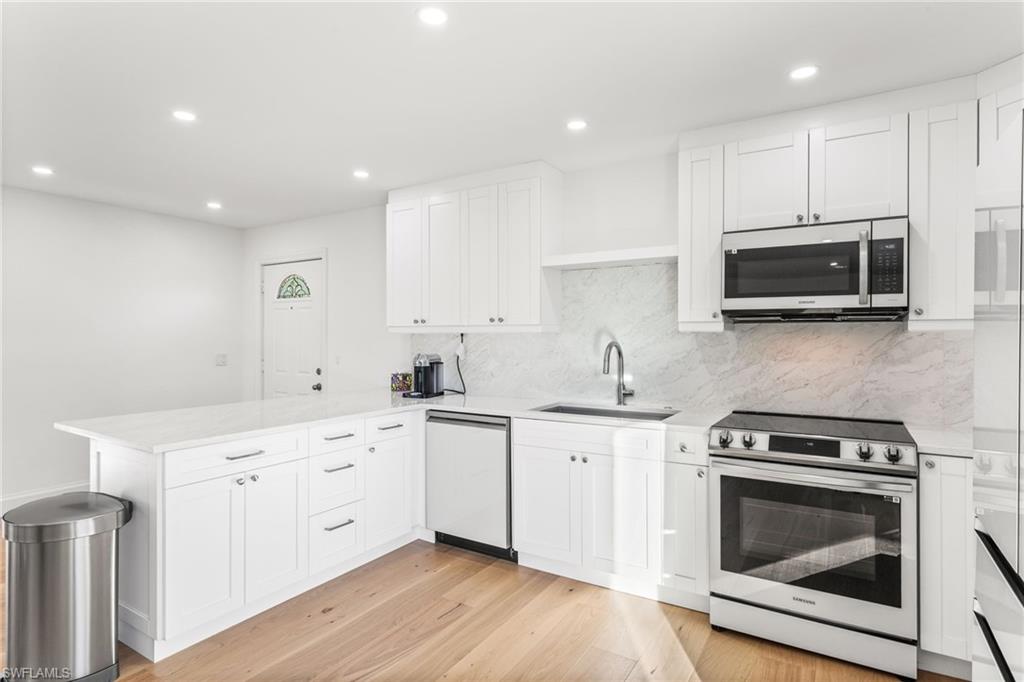 Kitchen with stainless steel appliances, white cabinetry, a peninsula, recessed lighting, and light wood flooring