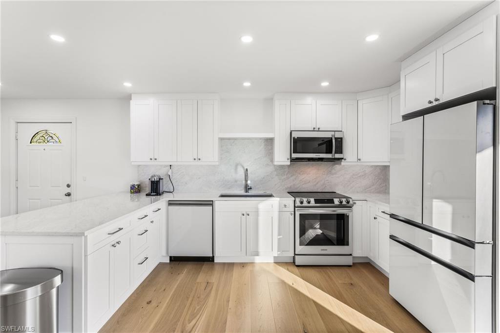 Kitchen with stainless steel appliances, white cabinetry, a peninsula, light stone countertops, and recessed lighting
