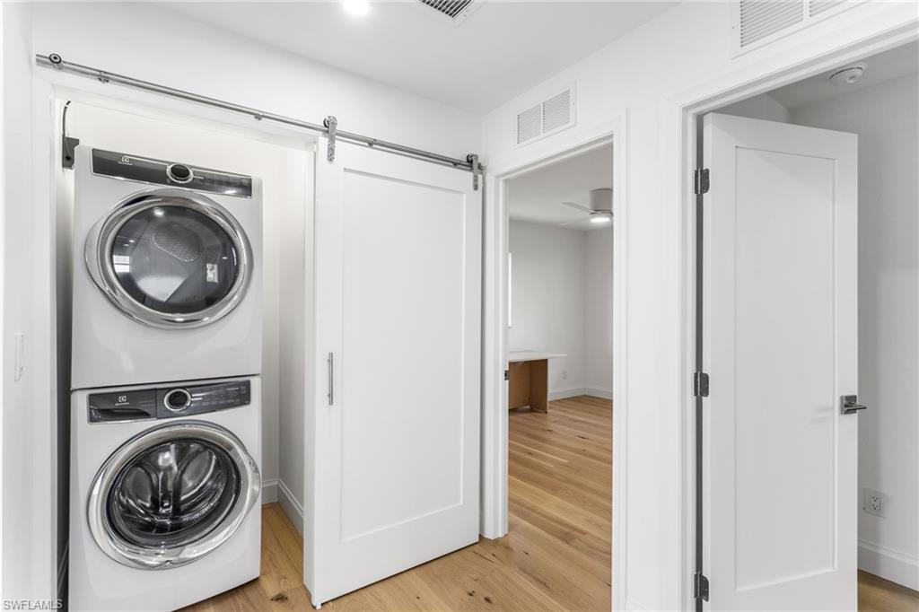 Laundry area featuring light wood flooring, stacked washer and clothes dryer, a barn door, and a ceiling fan