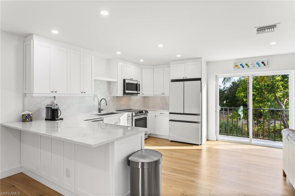 Kitchen featuring white cabinets, stainless steel appliances, a peninsula, light stone counters, and light wood flooring