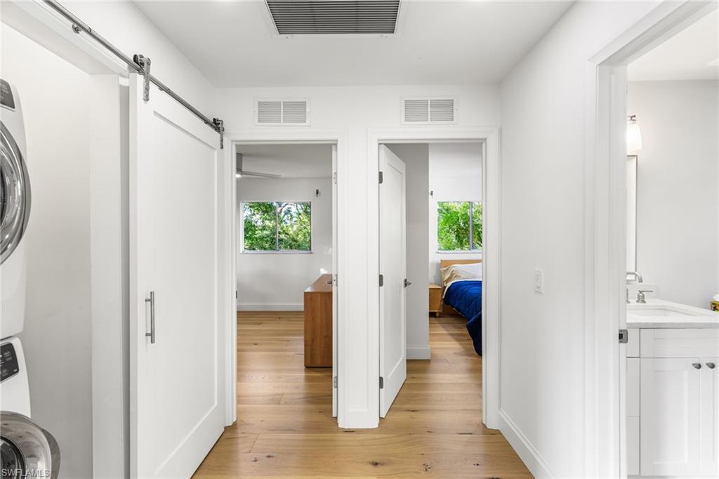 Corridor with a barn door, light wood flooring, and stacked washer / dryer