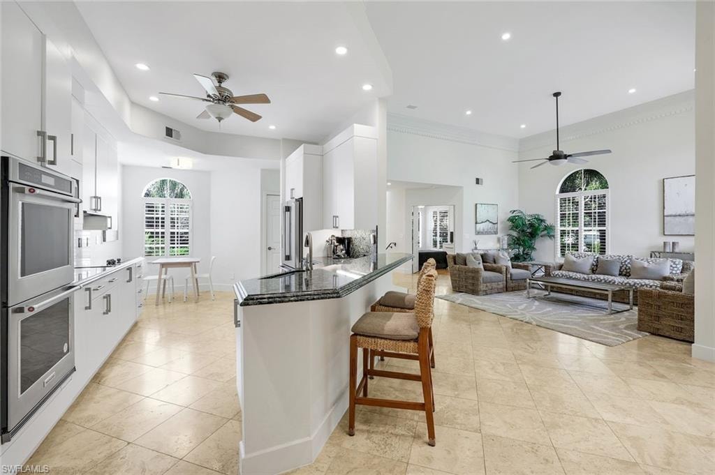 Kitchen with a ceiling fan, dark stone counters, appliances with stainless steel finishes, white cabinets, and a breakfast bar area