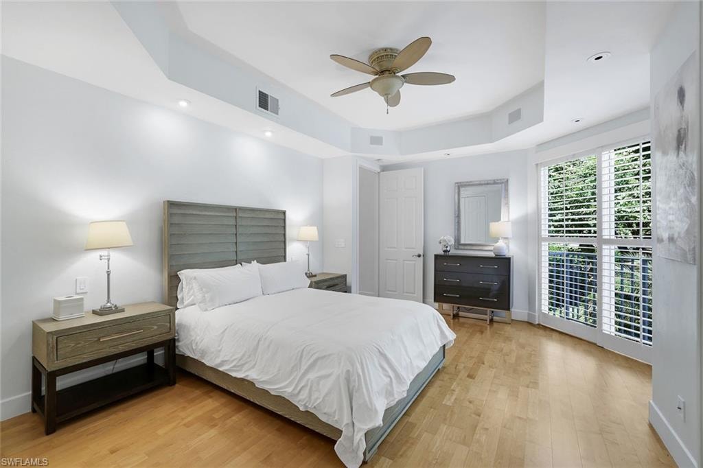 Bedroom with a tray ceiling, light wood-style floors, ceiling fan, and recessed lighting