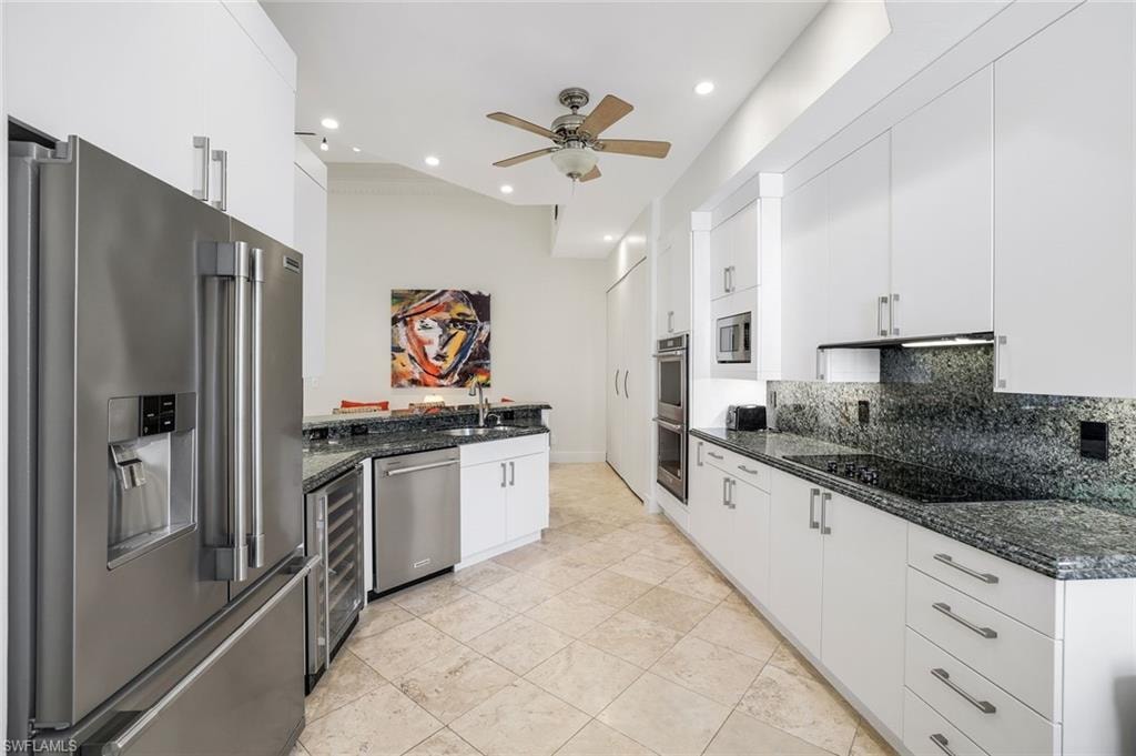 Kitchen with stainless steel appliances, dark stone countertops, white cabinetry, tasteful backsplash, and wine cooler