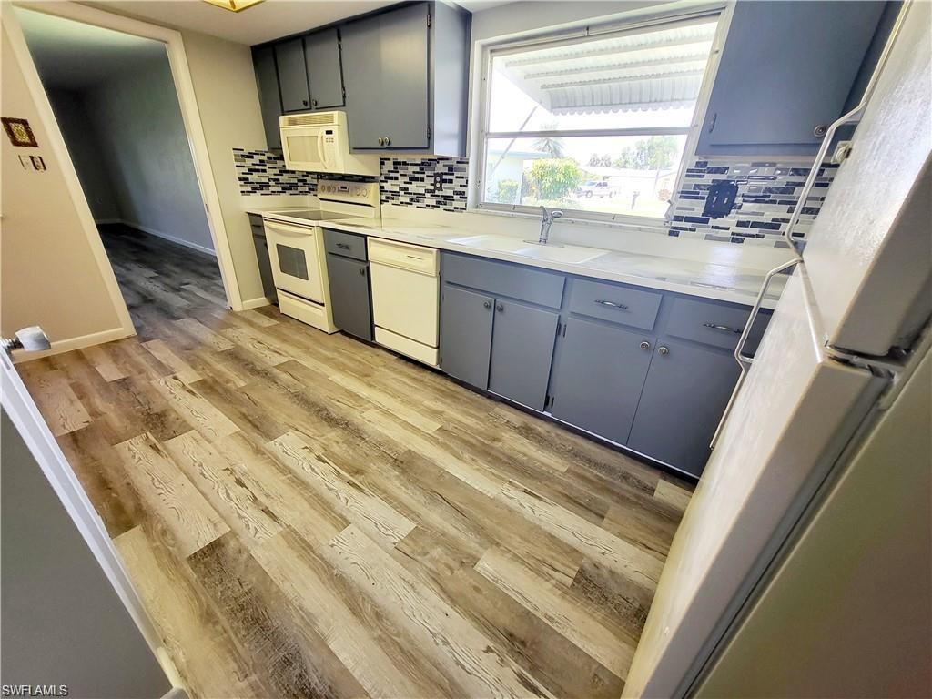 Kitchen with gray cabinets, white appliances, light countertops, light wood finished floors, and decorative backsplash
