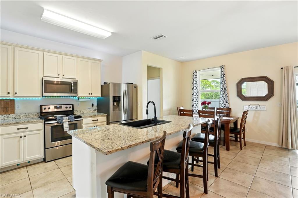 Kitchen featuring appliances with stainless steel finishes, cream cabinetry, a breakfast bar, and light stone countertops