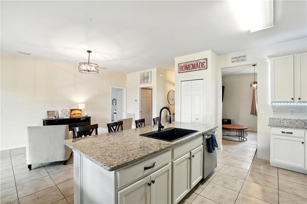 Kitchen with decorative light fixtures, white cabinetry, light stone counters, and a kitchen island with sink