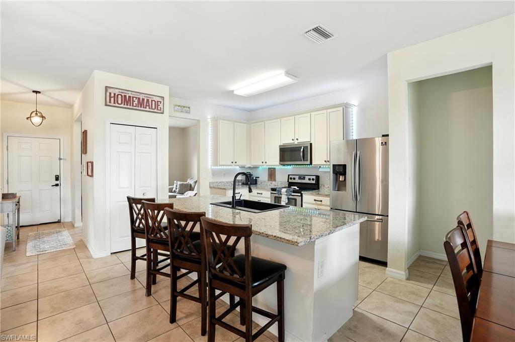 Kitchen featuring appliances with stainless steel finishes, light stone counters, light tile patterned floors, and an island with sink