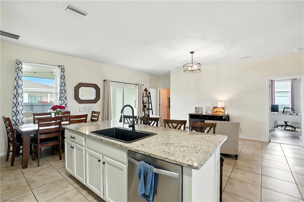 Kitchen featuring healthy amount of natural light, stainless steel dishwasher, an island with sink, and white cabinets