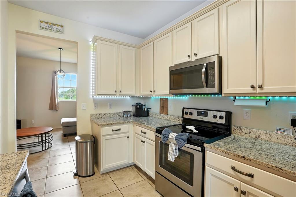 Kitchen featuring stainless steel appliances, light stone counters, light tile patterned floors, hanging light fixtures, and cream cabinets