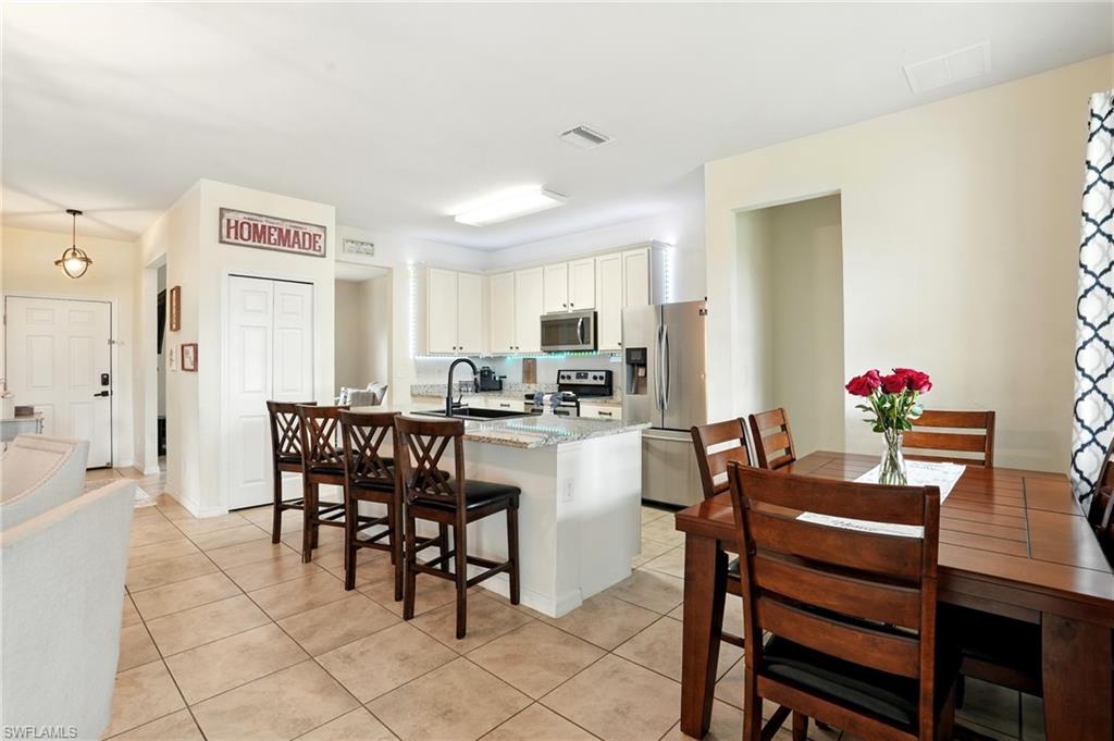 Kitchen with a center island with sink, stainless steel appliances, white cabinets, light stone countertops, and light tile patterned floors