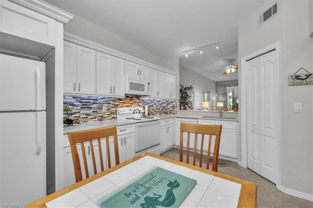 Kitchen with white cabinetry, white appliances, light tile patterned floors, ceiling fan, and backsplash