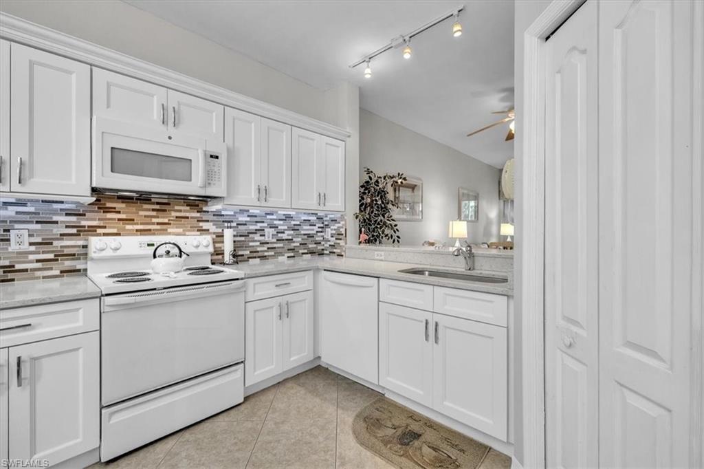 Kitchen with white appliances, white cabinetry, light tile patterned floors, light stone counters, and ceiling fan