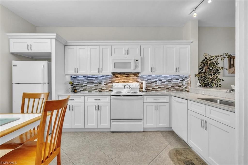 Kitchen featuring white appliances, white cabinetry, light stone counters, and tasteful backsplash