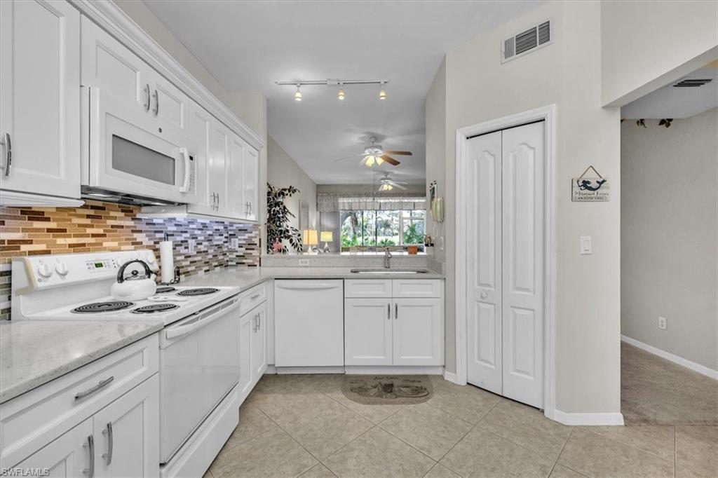 Kitchen featuring white appliances, white cabinets, light tile patterned floors, decorative backsplash, and ceiling fan