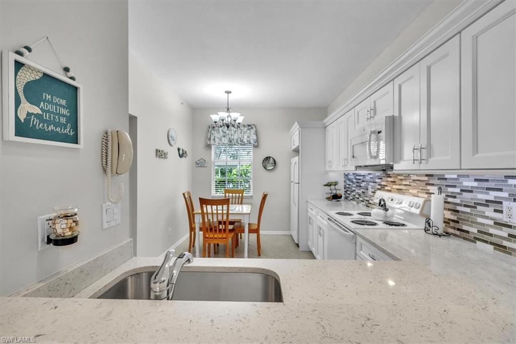 Kitchen featuring white appliances, white cabinetry, pendant lighting, tasteful backsplash, and light stone countertops