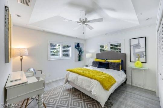 Bedroom featuring a tray ceiling, multiple windows, ceiling fan, and hardwood / wood-style flooring
