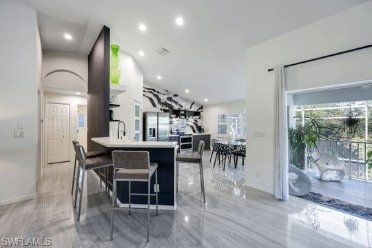 Kitchen with a kitchen bar, kitchen peninsula, stainless steel fridge with ice dispenser, and sink