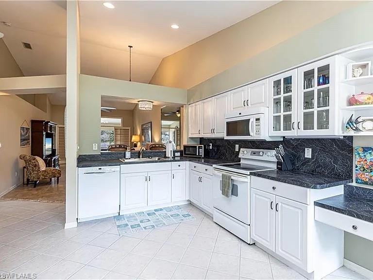 Kitchen with white appliances, white cabinetry, light tile patterned flooring, pendant lighting, and vaulted ceiling