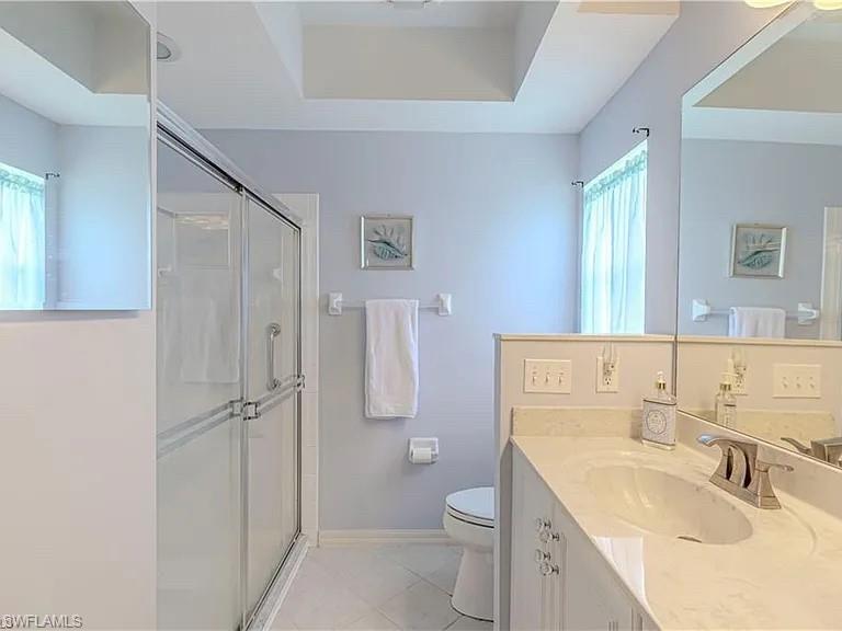 Bathroom with a shower stall, vanity, light tile patterned floors, and a tray ceiling