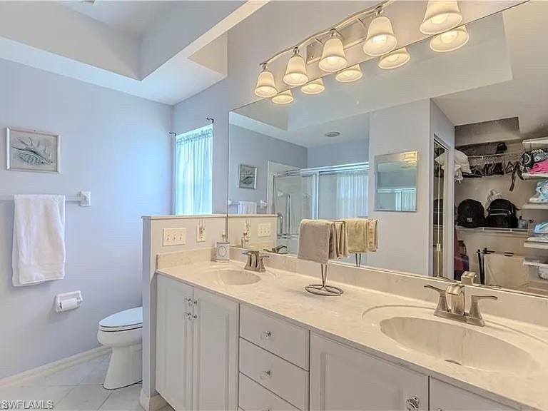 Bathroom with double vanity, a shower stall, a spacious closet, and light tile patterned floors
