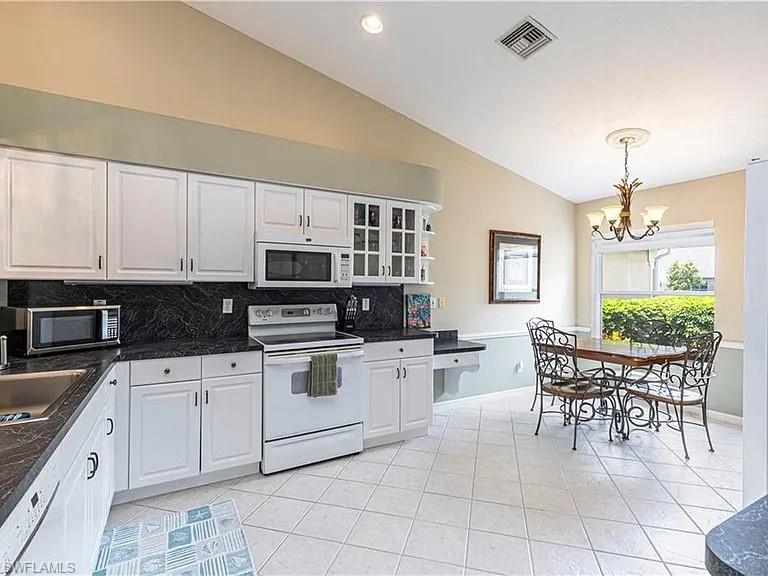 Kitchen featuring vaulted ceiling, white appliances, white cabinetry, decorative light fixtures, and backsplash