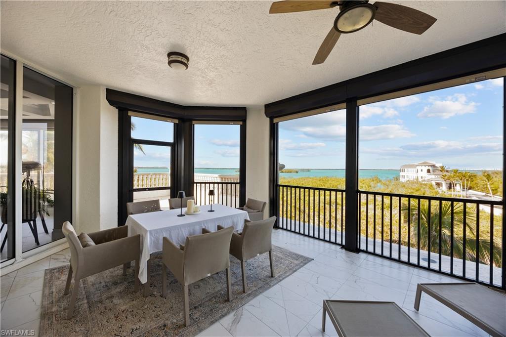 Sunroom with ceiling fan, a water view, and a beach view