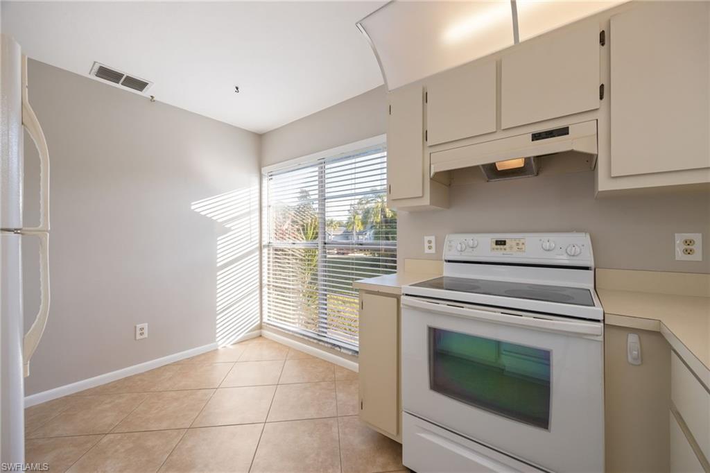 Kitchen with white appliances, light countertops, under cabinet range hood, light tile patterned floors, and cream cabinetry