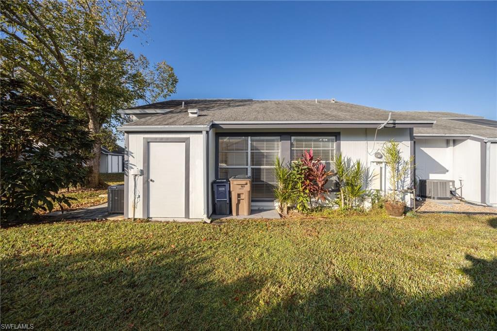Back of property with a lawn, roof with shingles, and a storage unit