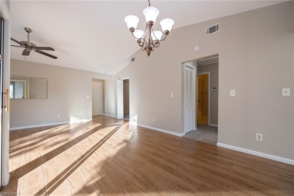 Empty room with wood finished floors, a chandelier, lofted ceiling, and a ceiling fan