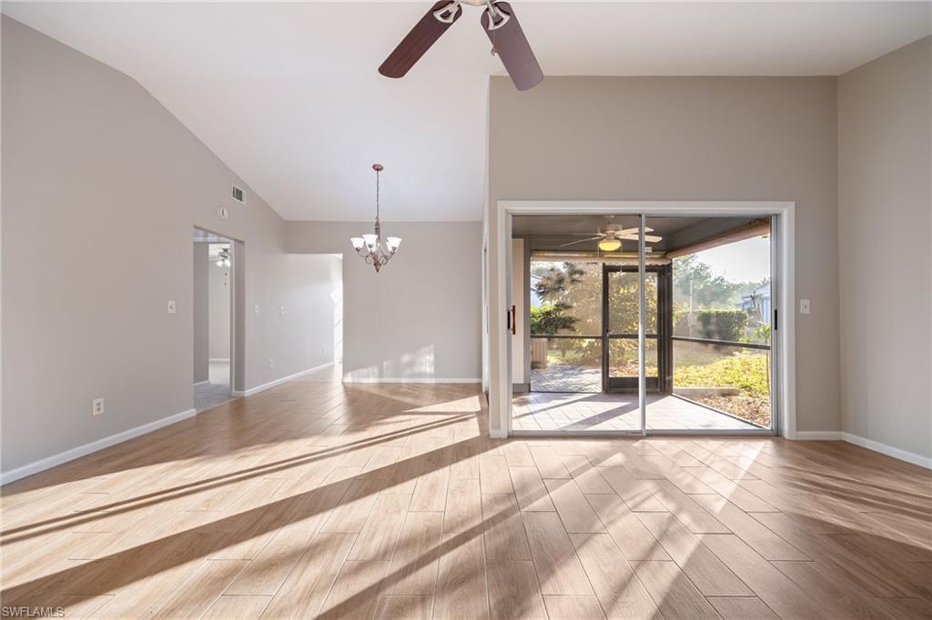 Empty room featuring a ceiling fan, wood tiled floors, a chandelier, and vaulted ceiling