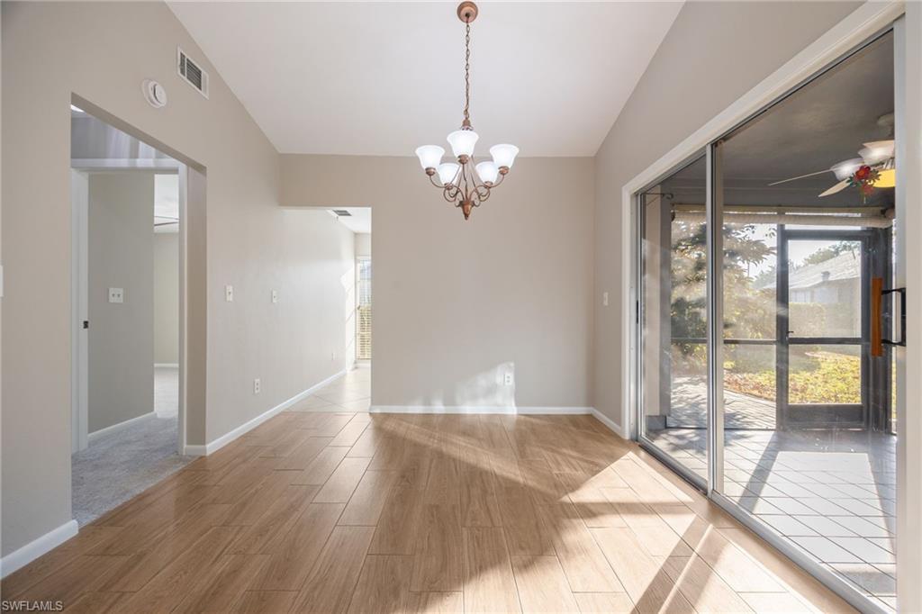 Unfurnished dining area with wood finish floors, a ceiling fan, a chandelier, and vaulted ceiling