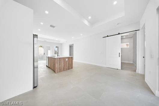 Unfurnished living room with a barn door, a raised ceiling, recessed lighting, and concrete flooring
