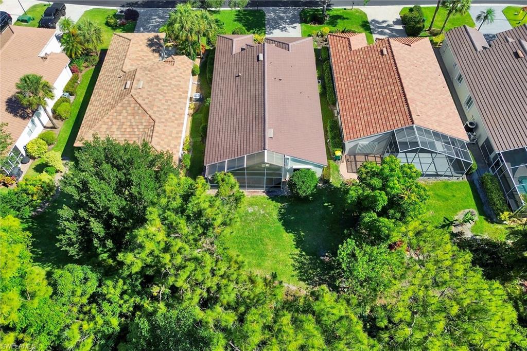 Aerial perspective showcasing a property with a brown shingle roof, green lawn space, and mature trees