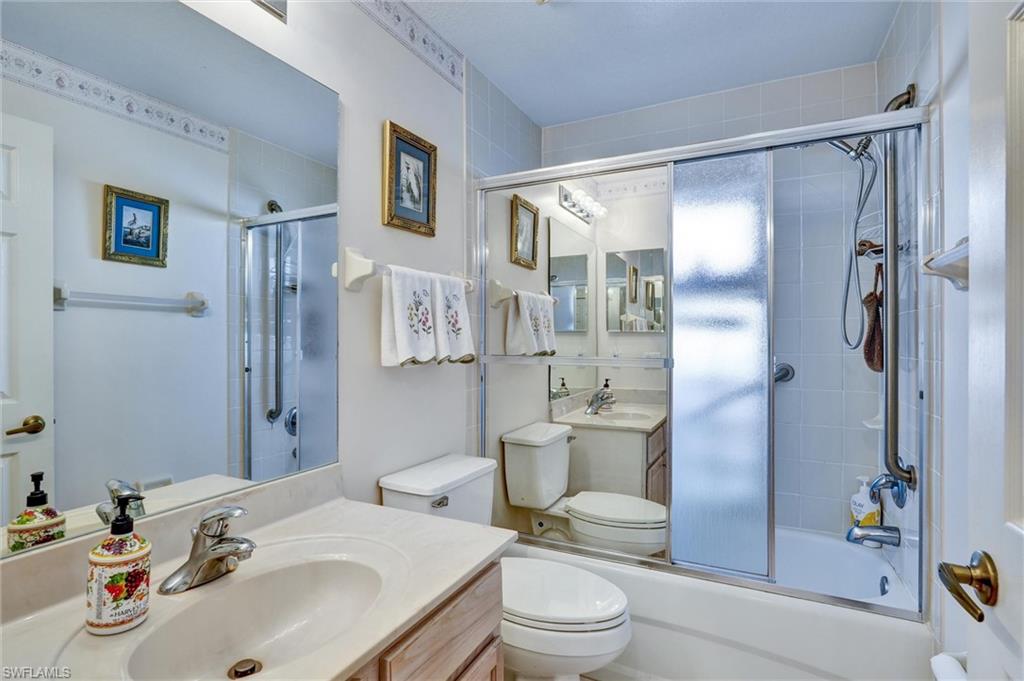 Full bathroom featuring a single vanity with an integrated sink, a large wall-mounted mirror, and a combination tub and shower with a sliding glass enclosure
