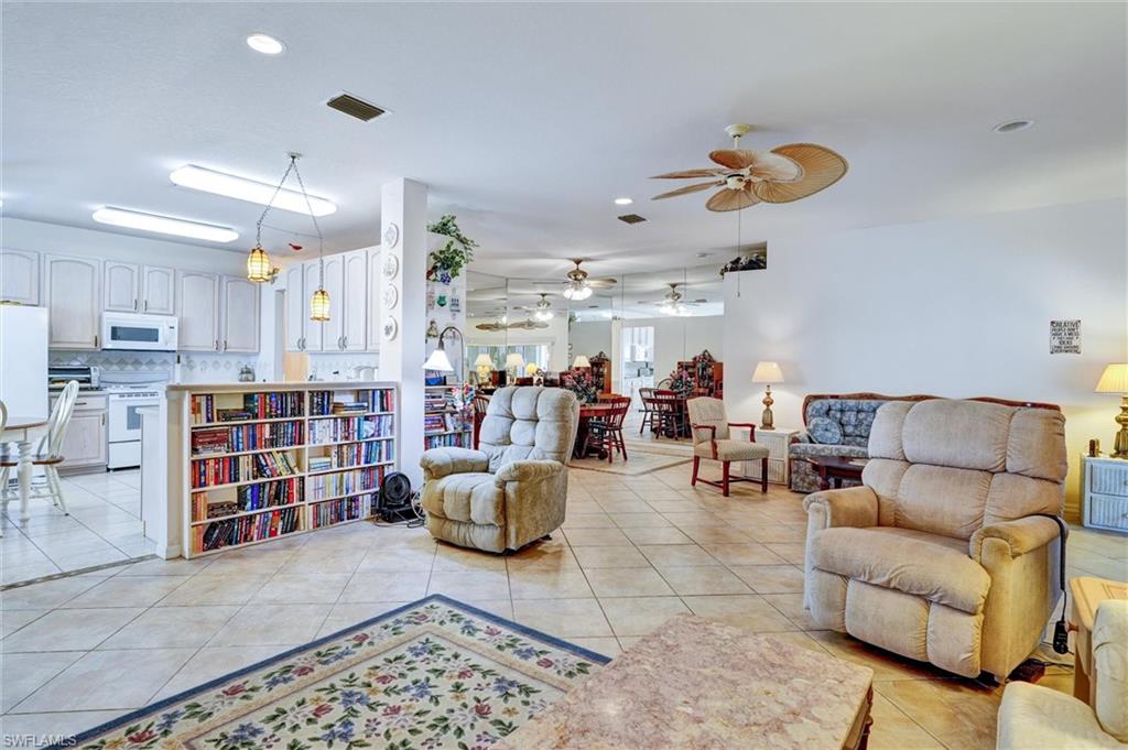 Open-concept living area featuring tile flooring, white kitchen cabinetry with pendant lighting, a built-in bookshelf island, and a ceiling fan