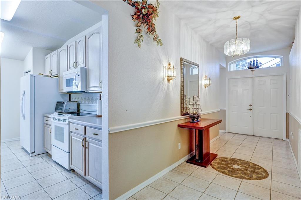 Foyer entrance with double entry doors and an arched transom window, featuring tiled flooring, a decorative chandelier, and wall sconces