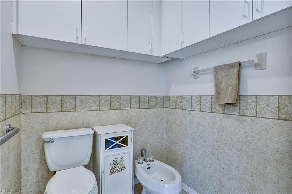 Bathroom featuring extensive white overhead cabinetry, a white toilet, and a bidet