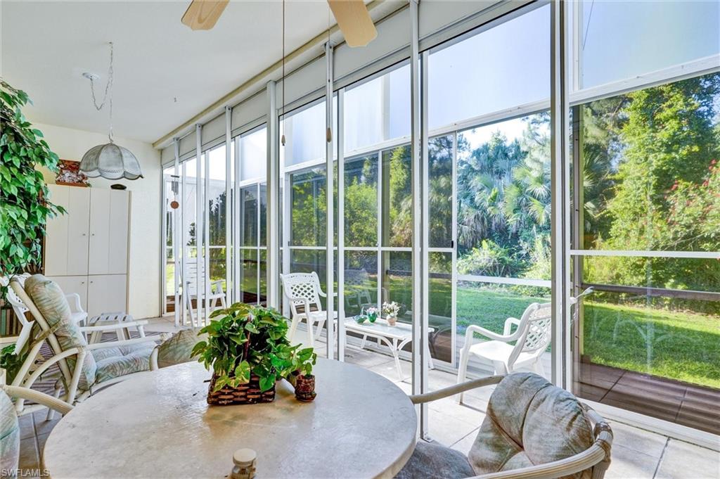 Screened lanai featuring white framing, multiple ceiling fans, a built-in storage unit, and a tiled floor