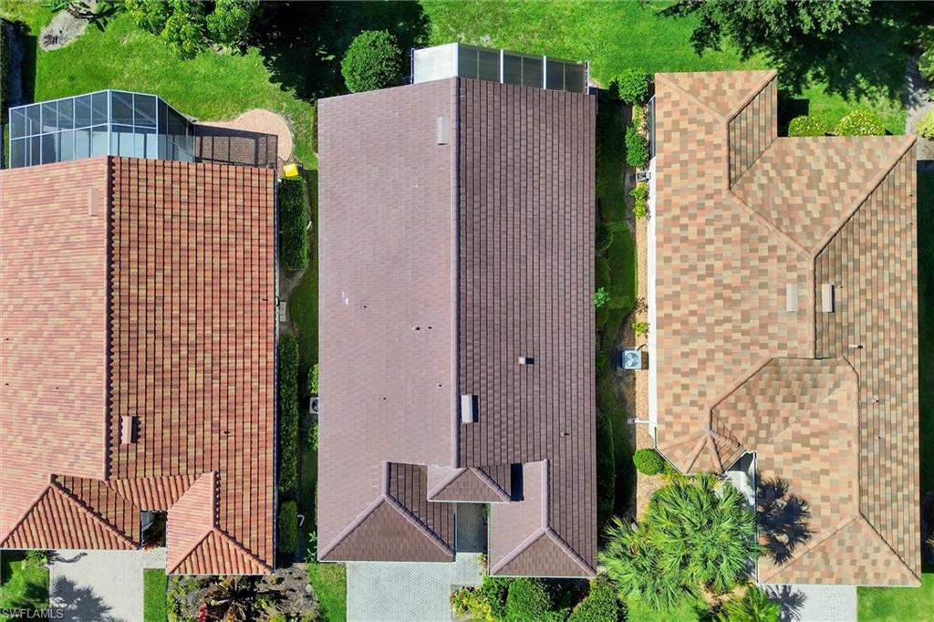 Aerial perspective showcasing a single-story residence with a brown shingle roof, accompanied by a paved driveway and surrounding green landscaping
