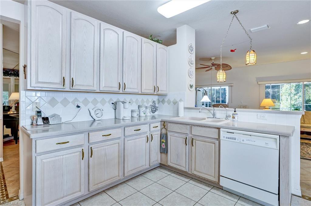 Kitchen featuring white cabinetry with brass hardware, light-toned countertops, and a white tile backsplash with decorative accents